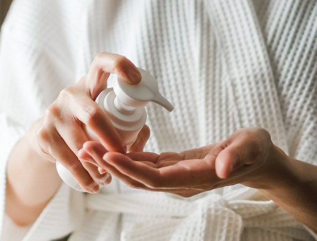 photo of person applying lotion to hand from pump bottle for skincare routine